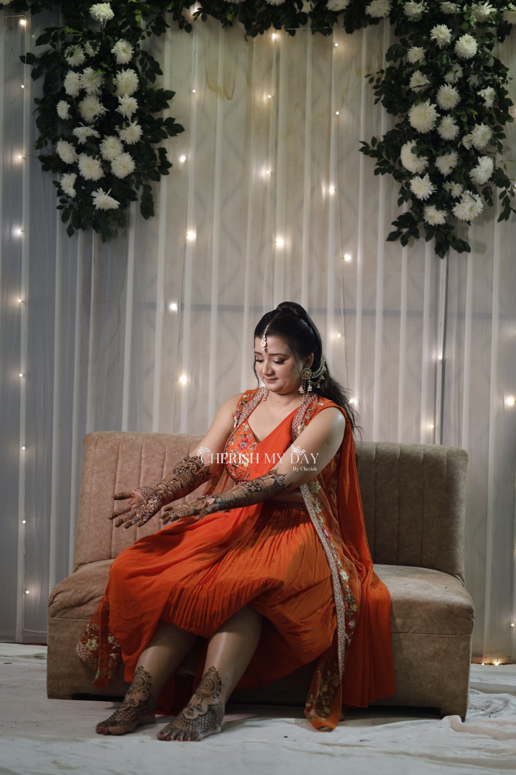 Beautiful bridal portrait in orange saree with elegant white floral backdrop and fairy lights